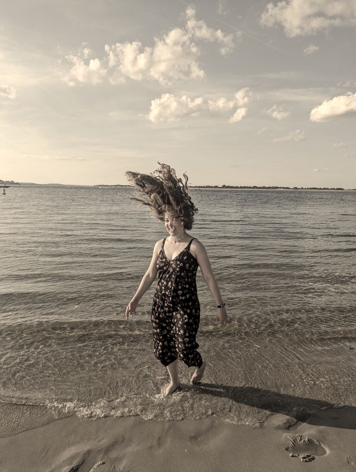 sepia toned image of caro, a girl standing ankle deep in the ocean and flipping her hair around.