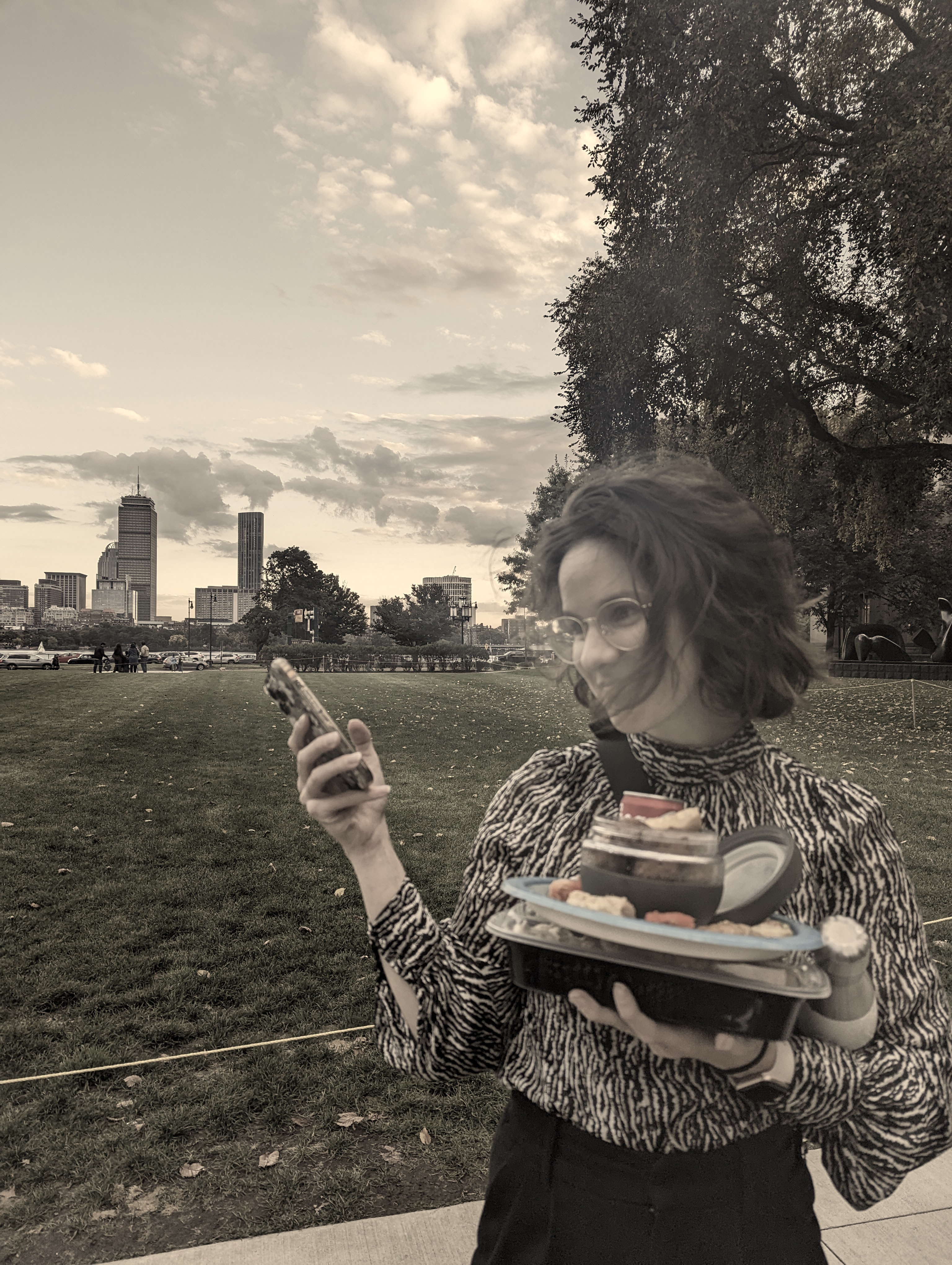 sepia toned image of lydia, a girl holding her phone and several containers of food.